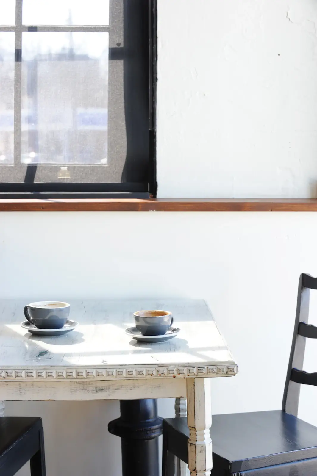Dos tazas de café sobre una mesa junto a una ventana con luz de la mañana